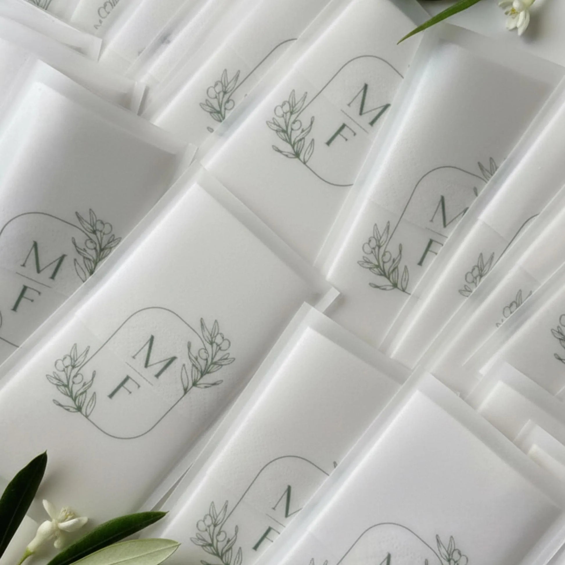 Mouchoir de mariage personnalisé dans une pochette en papier calque, décorée d’un monogramme vert entouré de délicates branches d’olivier. Design inspiré du sud de la France et de l’Italie, idéal pour un mariage méditerranéen, élégant et naturel. Accessoire raffiné pour invités ou cérémonie en plein air.